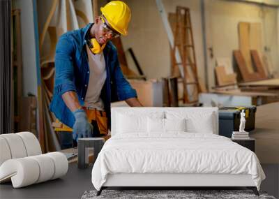 African American carpenter man use measure tape to check and work with timber in factory workplace and tools box is place on table near working area. Wall mural