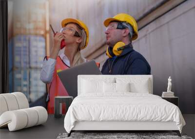 Beautiful technician or worker woman use walkie talky and work with engineer man in cargo container area with day light. Wall mural