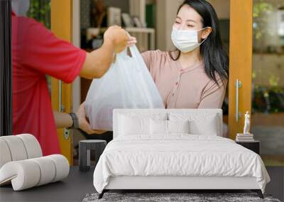 Beautiful woman with mask get delivery pizza or food from carrier man with red shirt and mask at home. Concept of new normal lifestyle to prevent virus infection during covid pandemic in city. Wall mural