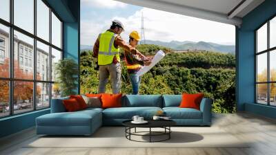 Engineer manager man discuss with his team who hold construction plan and stay in front of mountain view and  high voltage pole. Wall mural