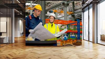 Factory workers man and woman discuss about the project using drawing paper or plan in workplace with machine and product shelves are in the background. Wall mural