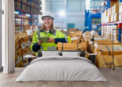 Pretty young warehouse woman hold tablet and stand near stack of product boxes in warehouse workplace and light on the background. Wall mural