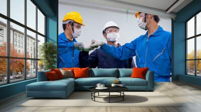 Three of factory workers men wearing mask stand with action of fighting and look to each other. Concept of encouragement for working in industrial workplace to win covid-19 virus pandemic. Wall mural