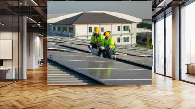 Two Caucasian technician workers use construction plan and tablet to check and maintenance solar cell panels on rooftop of factory or the building. Green and sustainable energy for good environment. Wall mural