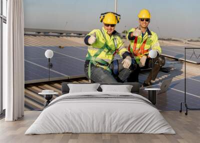 Two industrial technician worker sit near solar cell panels on rooftop of factory building and show thumbs up to camera with smiling. Green and sustainable energy concept. Wall mural