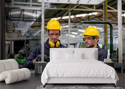 Two technician men with blue uniform and yellow helmet work with the machine in factory. Wall mural