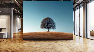 A lone tree stands in a field of grass. The sky is clear and blue, and the tree is the only object in the scene. Scene is peaceful and serene, as the tree stands alone in the vast open field Wall mural