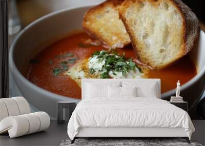 A bowl of steaming tomato soup, topped with a dollop of creamy ricotta cheese and fresh herbs, served with two slices of toasted bread. A classic comfort food with a touch of elegance. Wall mural