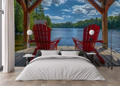 View of two red adirondack chair on a wooden dock from a cottage's boathouse Wall mural