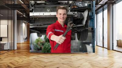 Auto mechanic in red uniform standing at car repair station holding wrench prepare to fix broken engine vehicles at mechanics garage. Smiling maintenance engineer happy work in automotive industry Wall mural