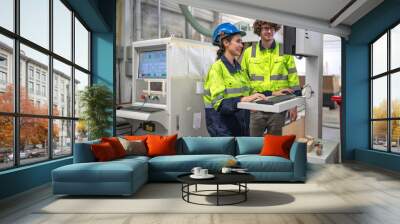 Industrial engineer wear helmet and safety uniform working in heavy engineering factory. Confident technician woman and colleague worker operating automated machine in manufacturing facility workshop Wall mural