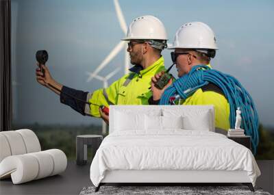 Maintenance engineer team standing at windmills at wind turbine farm. Group of people wear safety helmet and uniform working at alternative renewable energy wind station. Sustainable energy technology Wall mural