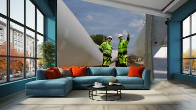 Maintenance engineer team standing at windmills at wind turbine farm. Group of people wear safety helmet and uniform working at alternative renewable energy wind station. Sustainable energy technology Wall mural