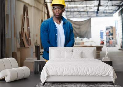 Male carpenter standing in carpentry workshop. A multiracial repairman at work in wood furniture building factory. Portrait of joiner man with protective gear worker standing in woodwork manufacturing Wall mural