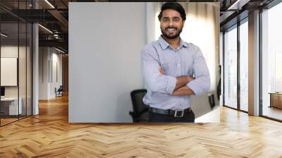 Portrait of indian businessman happy standing arms crossed in modern office. Confident young smart bearded man entrepreneur looking at camera smiling. Friendly india ethnic manager work in workplace. Wall mural