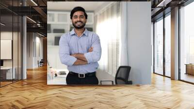 Portrait of indian businessman happy standing arms crossed in modern office. Confident young smart bearded man entrepreneur looking at camera smiling. Friendly india ethnic manager work in workplace. Wall mural