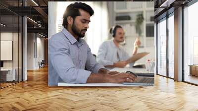 Success Indian businessman sitting in modern office using laptop computer. Confident professional entrepreneur serious working at workplace. Successful India ethnic executive enjoy his corporate job Wall mural