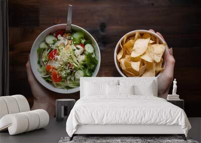 One hand holding bowl of vegetable salad, other holding chips. Healthy natural organic fresh vegetarian food choice vs unhealthy processed fast junk food. Lunch or snack decision green meal dieting Wall mural