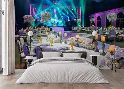 Long dinner table decorated with white flowers, shiny candles and golden glasses stands in a beautiful hall Wall mural