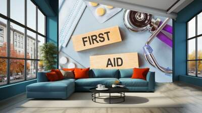 FIRST AID phrase on two wooden blocks on doctors table with stethoscope, white and yellow pills and medical face mask. Wall mural