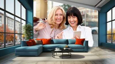 Two mature women looking at the phone and having fun while doing shopping Wall mural