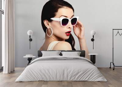 Fashion studio closeup portrait of gorgeous elegant surprising woman in white sunglasses and fashion earrings posing on blue wall background with empty copy space Wall mural