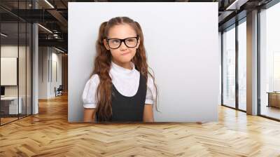 Grimacing  pupil girl with long hair style in fashion eyeglasses in uniform making fun physiognomy on blue background with empty copy space. Wall mural