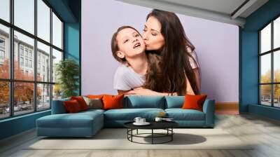 Happy excited mother cuddling and kissing her daughter on purple background with empty copy space. Natural emotional family. Wall mural