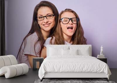 Happy young casual mother and smiling kid in fashion glasses hugging on purple background with empty copy space. Wall mural