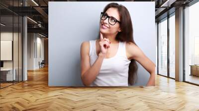 Healthy young thinking woman in glasses looking up on blue backg Wall mural