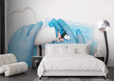 Hands in the blue medical gloves hold an jar of pills, protective mask and stethoscope lie on the white background. Wall mural