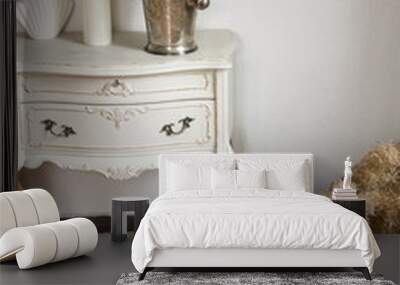 old vintage white commode with fluffy plant and decoration on it is standing near the white wall background on the parquet floor. interior details in french apartment, free space Wall mural