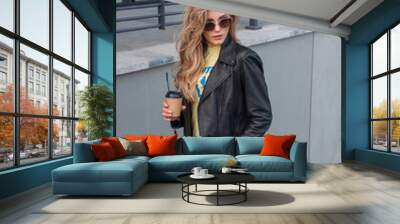 teen walk leisure. young blonde girl in jeans and black leather jacket stands in step on gray street stairs background with coffee in hand and looks apart in sunglasses. lifestyle concept, free space Wall mural