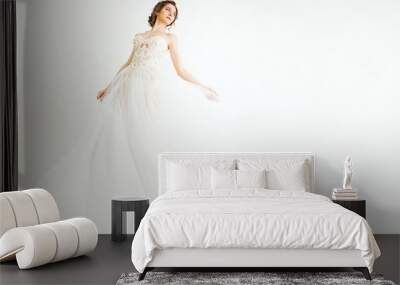 young smily brunette sexy girl in a white wedding boudoir dress and crown in hairstyle is dancing  like swan princess in motion  on a white wall background  Wall mural