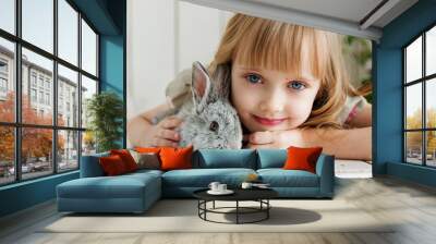 Cute girl hugging with rabbit while lying on the floor at home Wall mural