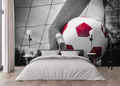 black and white close up image  of an arm of a man holding a red and white soccer ball against his thigh with the net in the background. Wall mural