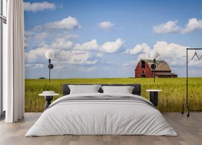 old abandoned red barn sitting in a field of green grass under a blue sky filled with white clouds Wall mural