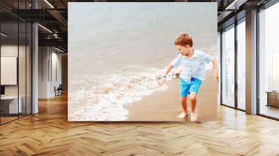 little boy in shirt and shorts on the beach sand. Little boy having fun on tropical ocean beach. Kid during family vacation. Summer water fun. Wall mural