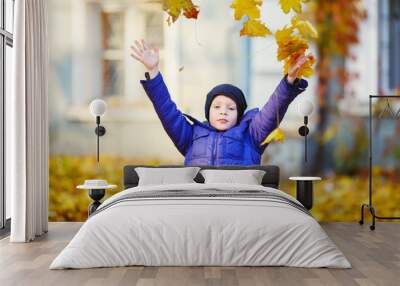 Portrait of happy joyful beautiful little boy outdoors at the autumn. Child holding a yellow maple leaves. Wall mural