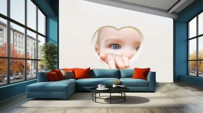 baby face, eyes and hand peep out of a heart-shaped hole in the center. A child looks into the camera through a heart hole. Love and health concept, mock up, poster, Wall mural