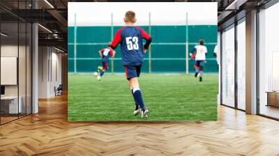 Boys in white and blue sportswear plays  football on field, dribbles ball. Young soccer players with ball on green grass. Training, football, active lifestyle for kids concept  Wall mural