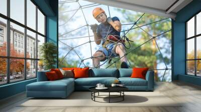 Sporty, young, cute boy in white t shirt spends his time in adventure rope park in helmet and safe equipment in the park in the summer. Active lifestyle concept, summer camp Wall mural