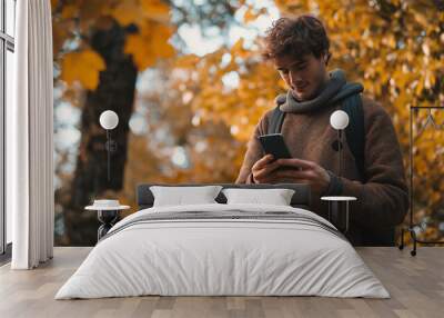 Young man using a smartphone in autumn, happy lifestyle, online texting, communication with a phone in hand, as a male mobile user, enjoying the outdoor nature Wall mural