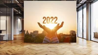 2022 is supported by hands on the background of a sunny sunset. Wall mural