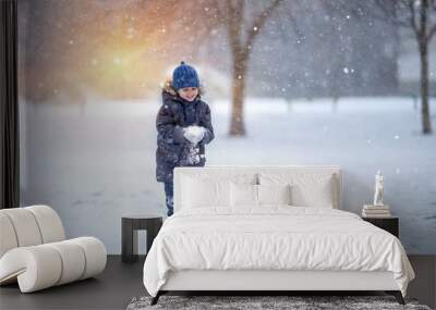 A little boy in a hat and jacket laughs and rejoices in the winter snow . Wall mural