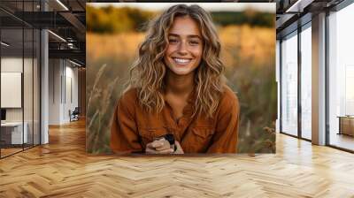 A woman smiles warmly while holding a product in a sunlit field during golden hour, capturing the essence of a casual outdoor photoshoot Wall mural