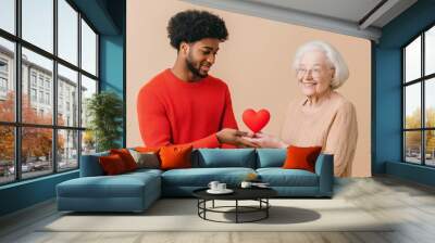 A young man gives a heart to a smiling elderly woman, showcasing warmth and connection in a bright setting Wall mural