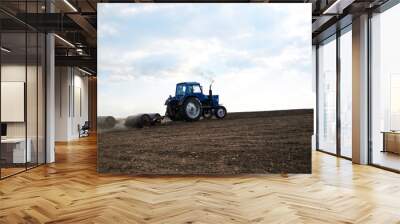 Agricultural work on field with black soil. Blue tractor riding and seeding countryside. Rural works in spring. Environmental protection concept. Ecological products cultivation. Natural background. Wall mural