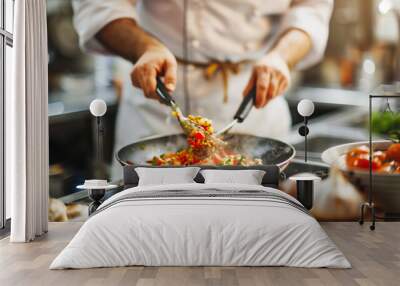 Chef cooking a colorful vegetable stir-fry in a professional kitchen, using tongs to stir ingredients in a hot pan. Fresh tomatoes and garlic are in the foreground. Wall mural