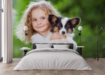 Little curly girl with a papillon puppy, outdoor summer Wall mural